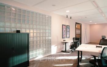 Modern office space with desks, chairs, and a glass block wall at Jachthavenweg 109-A, Amsterdam Zuidas.