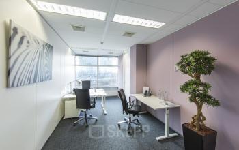 Modern office space rental at Zuidplein 36, Amsterdam Zuidas, featuring a well-lit room with desks, chairs, and a decorative plant.