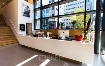 Spacious reception area with large windows and modern decor at Barbara Strozzilaan 101-201, ideal for office space rental in Amsterdam Zuidas. A person is working at the reception desk.