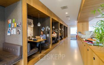 Modern office with booths at Barbara Strozzilaan 101-201 in Amsterdam Zuidas, ideal for office space rental. Professionals working on laptops in a collaborative environment.