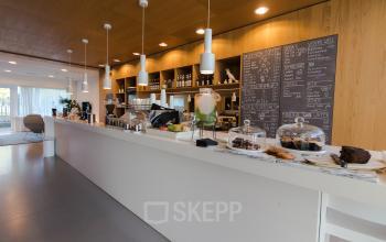 A stylish cafe area in an office space rental at Barbara Strozzilaan 101-201, Amsterdam Zuidas, featuring a long counter with pastries and coffee equipment, ideal for breaks and casual meetings.