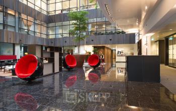 Modern office space rental at Strawinskylaan 3051, Amsterdam Zuidas, featuring stylish red chairs and polished floors.