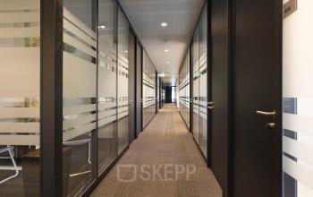 Modern corridor with glass-walled offices offering a professional atmosphere for office space rental at Strawinskylaan 3051, Amsterdam Zuidas.