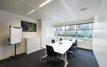 Modern office space rental at Strawinskylaan 3051, Amsterdam Zuidas, featuring a neat conference room with a large window and a screen for presentations.