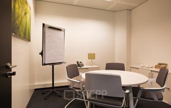 Modern conference room available for office space rental at Strawinskylaan 3051, Amsterdam Zuidas, with round table, chairs, and presentation board.