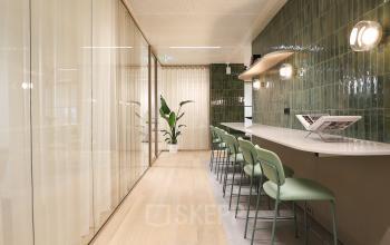 Modern office to rent at Beethovenstraat 503, Amsterdam Zuidas featuring a sleek, furnished workspace with green chairs and tiled walls, ideal for office space rental.