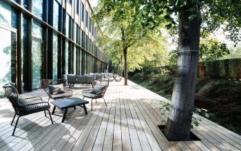 Outdoor seating area with modern furniture and greenery alongside an office building at Fred. Roeskestraat 115 in Amsterdam Zuidas, ideal for breaks or informal meetings. Perfect blend of nature and professional space.