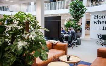 Modern office space at Fred. Roeskestraat 115, Amsterdam Zuidas features a stylish lounge with leather couches and bustling workstations where professionals engage in collaborative tasks. Ideal for office space rental.
