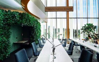 Modern workspace at Fred. Roeskestraat 115, Amsterdam Zuidas, featuring a row of sleek desks under a skylight, with green plant walls adding a natural touch. Ideal for office space rental.