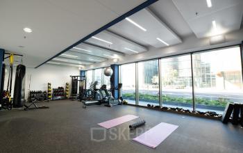 A spacious interior gym area at Fred. Roeskestraat 115 in Amsterdam Zuidas, equipped with modern fitness machines and mats facing large windows.