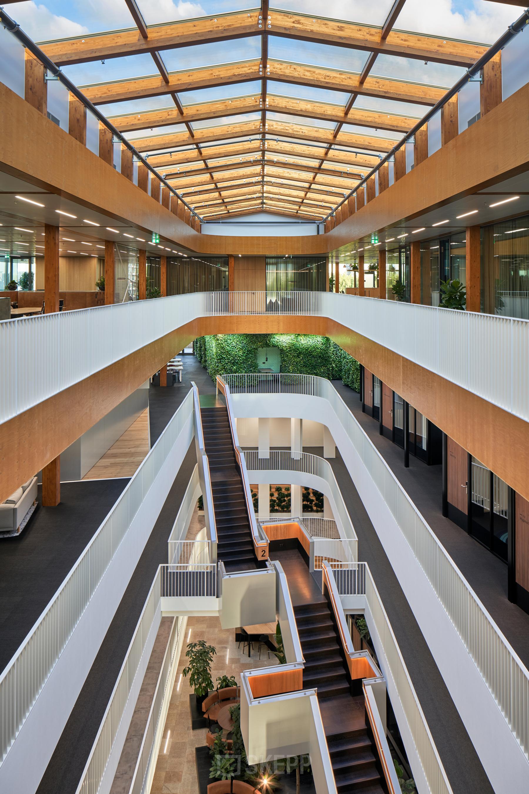 Bright, modern office interior at Fred. Roeskestraat 115 in Amsterdam Zuidas, featuring a multi-level atrium with large skylights, plants, and staircases. Ideal for office space rental.