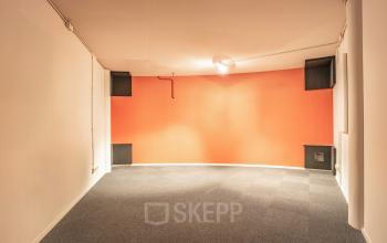 An empty office space with a curved, orange accent wall and carpet flooring at De Boelelaan 1110, ideal for office space rental in Amsterdam Zuidas.