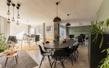 Bright office space for rent in Amsterdam Zuidas with modern furnishings, featuring workstations, a long table, and natural light from large windows.