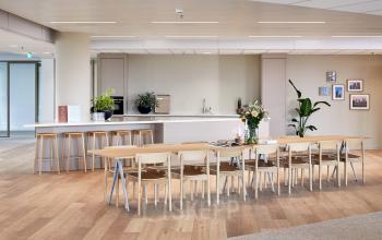 Spacious furnished office area in Amsterdam Zuidas, featuring a long table with chairs, bar stools, and a kitchenette. Ideal for office space rental at Hildegard Von Bingenstraat 44.