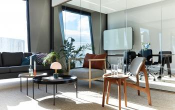 Modern office space for rent in Amsterdam Zuidas with stylish furniture, glass walls, and natural light through large windows. Ideal for office space rental with comfortable seating and plants.