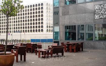 Outdoor seating area at Barbara Strozzilaan 101, Amsterdam Zuidas, featuring wooden benches and tables, ideal for breaks or informal meetings. Discover office space rental options for your business needs.