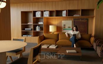 Comfortable office lounge in Amsterdam Zuidas with stylish wooden furniture and person reading, ideal for office space rental.