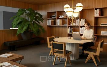 A furnished office at Barbara Strozzilaan 101, Amsterdam Zuidas, features wooden decor, bookshelves, a round table, and a person working on a laptop. Ideal for office space rental.