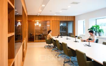 Modern office space at Barbara Strozzilaan 101, Amsterdam Zuidas, featuring a well-lit conference room with large table, office chairs, and two people working on laptops.