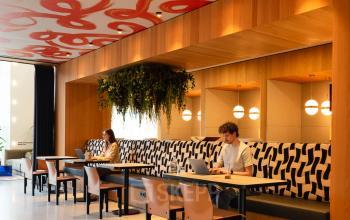 Bright office space with modern seating areas, artistic ceiling design, and individuals engaged in work at Barbara Strozzilaan 101, Amsterdam Zuidas. Ideal for rent office space.