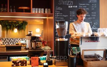 Man working at a coffee bar inside an office space at Barbara Strozzilaan 101, Amsterdam Zuidas. The setting offers a cozy environment for office space rental.