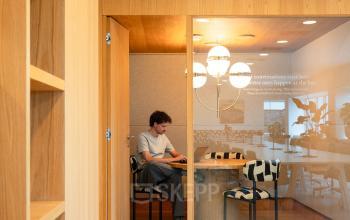 Office space at Barbara Strozzilaan 101, Amsterdam Zuidas. A person is working on a laptop in a furnished meeting area with wooden accents, ideal for office space rental.