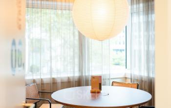 Cozy office space with a round table and four chairs under a large hanging lamp at Barbara Strozzilaan 101, Amsterdam Zuidas, ideal for small meetings. Perfect spot for office space rental.