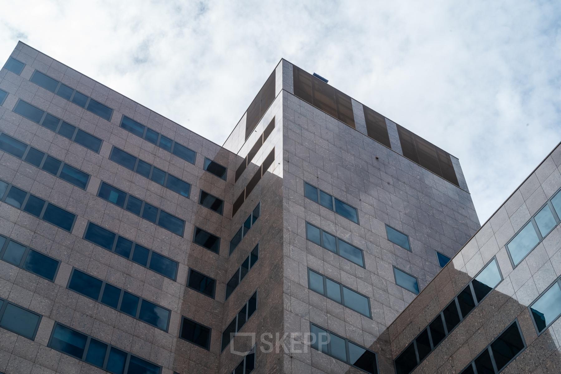 A tall, modern office building with a geometric design at Barbara Strozzilaan 101, perfect for those seeking office space rental in Amsterdam Zuidas.