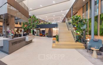 Modern interior view of an office space for rent in Amsterdam Zuidas, featuring a spacious open floor plan with greenery, comfortable seating, and a welcoming ambiance.