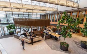 Interior of a modern office space at Jachthavenweg 109, Amsterdam Zuidas, with a reception area and people interacting and working.