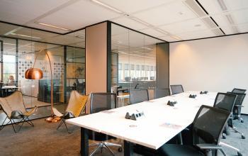 Modern office space in Amsterdam Zuidas with large conference table, comfortable chairs, and glass walls. Ideal for office space rental at Jachthavenweg 109.
