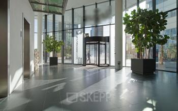 Spacious entrance lobby at Gustav Mahlerplein 2, Amsterdam Zuidas with large glass windows, potted plants, and a revolving door.