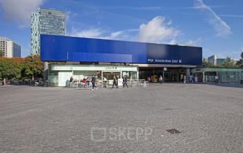 Exterior view of Amsterdam Zuid office building located at Gustav Mahlerplein 2, in Amsterdam Zuidas, with a few people walking and sitting outside.