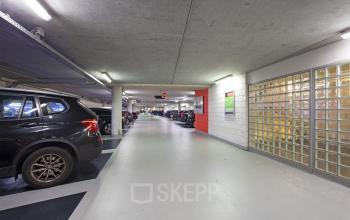 Underground parking area at Gustav Mahlerplein 2, Amsterdam Zuidas, Amsterdam, with various parked cars and bright overhead lighting.