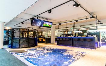 Bright, furnished office space available for rent at Gustav Mahlerplein in Amsterdam Zuidas, featuring a stylish open floorplan with a vibrant blue carpet and modern seating area.
