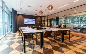 Modern office space for rent at Claude Debussylaan 7-29, Amsterdam Zuidas, featuring a stylish meeting area with geometric flooring, glass partitions, and trendy light fixtures.