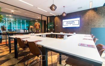 Modern conference room at Claude Debussylaan 7-29, Amsterdam Zuidas, featuring stylish decor, long tables, and a wall-mounted screen. Ideal for office space rental.