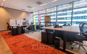 Modern office space with large windows and multiple workstations available for rent at Claude Debussylaan 7-29, Amsterdam Zuidas. The bright interior features desks and chairs, ideal for office space rental.