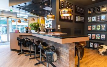 A stylish workspace at Claude Debussylaan 7-29, Amsterdam Zuidas, featuring a bar-style table with saddle stools, plants, and decorative lighting, ideal for office space rental.