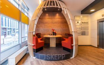 Cozy office space rental in Amsterdam Zuidas featuring a unique circular seating area with red cushioned benches and a wooden table, perfect for collaborative work sessions.