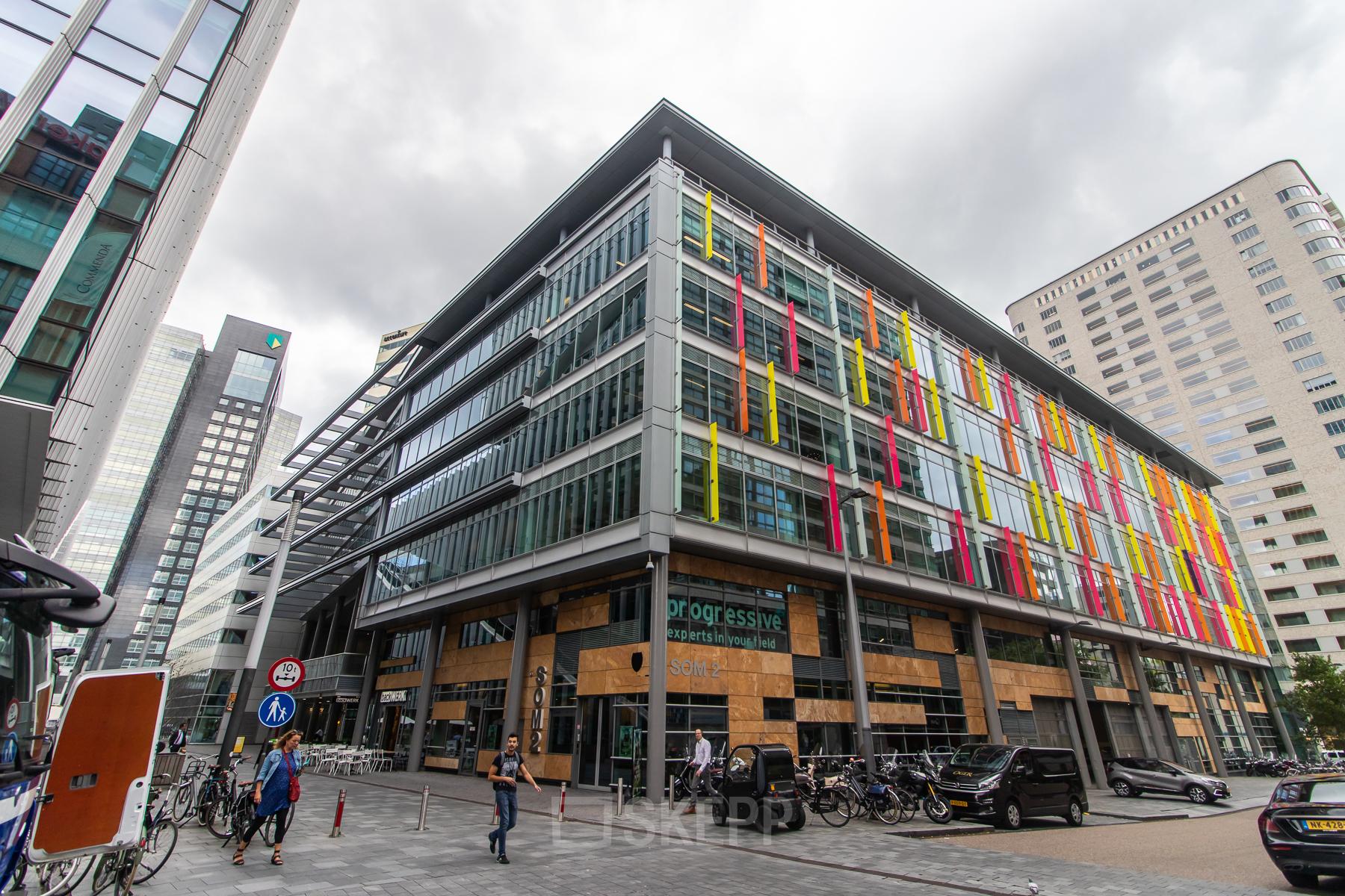 Exterior view of the office building at Claude Debussylaan 7-29, Amsterdam Zuidas, showcasing colorful facades and bicycles nearby, ideal for office space rental.