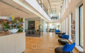 Modern office space rental at Gustav Mahlerplein 109-115 in Amsterdam Zuidas featuring open floorplan with glass-walled meeting rooms, plush seating, and contemporary decor.