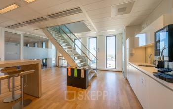Modern office space rental at Gustav Mahlerplein 109-115, Amsterdam Zuidas, featuring glass partitions, wooden floors, a kitchenette, and natural light from floor-to-ceiling windows.