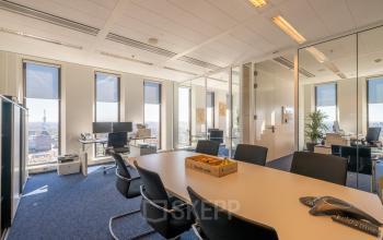 Modern office space at Gustav Mahlerplein 109-115, Amsterdam Zuidas, with a large meeting table, ergonomic chairs, and panoramic windows offering city views.
