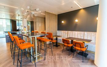 Modern office lounge area with orange chairs and high tables at Gustav Mahlerlaan 1212, Amsterdam Zuidas, ideal for office space rental.