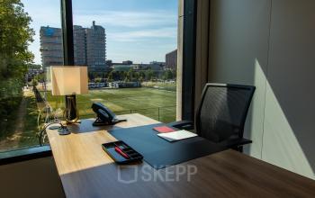 Modern office to rent at Gustav Mahlerlaan 1212, Amsterdam Zuidas featuring a desk, chair, lamp, and phone with a window view of the city.