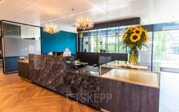 Modern reception area with marble desks, elegant lighting fixtures, and vibrant sunflowers in an office located at Gustav Mahlerlaan 1212, in Amsterdam Zuidas, available for office space rental.