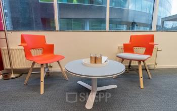 Zakelijke ruimte met twee rode stoelen en een ronde tafel bij het raam in een kantoor te huur op Uitbreidingstraat 84, Antwerpen Berchem.