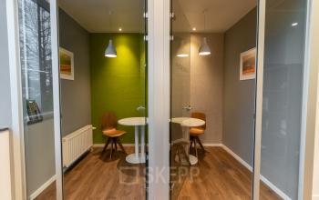 Vergaderruimte met glazen wanden en houten vloer op Uitbreidingstraat 84, Antwerpen Berchem. Twee houten stoelen en een witte tafel voor zakelijke gesprekken.