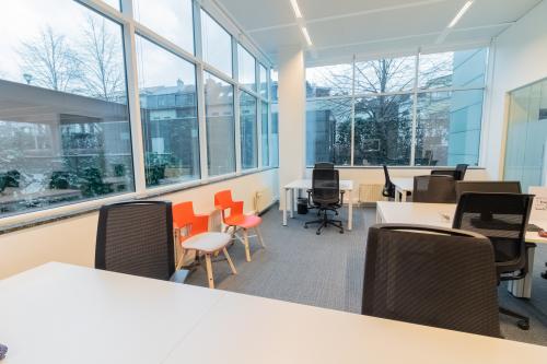 Bright office space rental at Uitbreidingstraat 84 in Antwerp Berchem, featuring modern desks, chairs, and large windows letting in ample natural light.